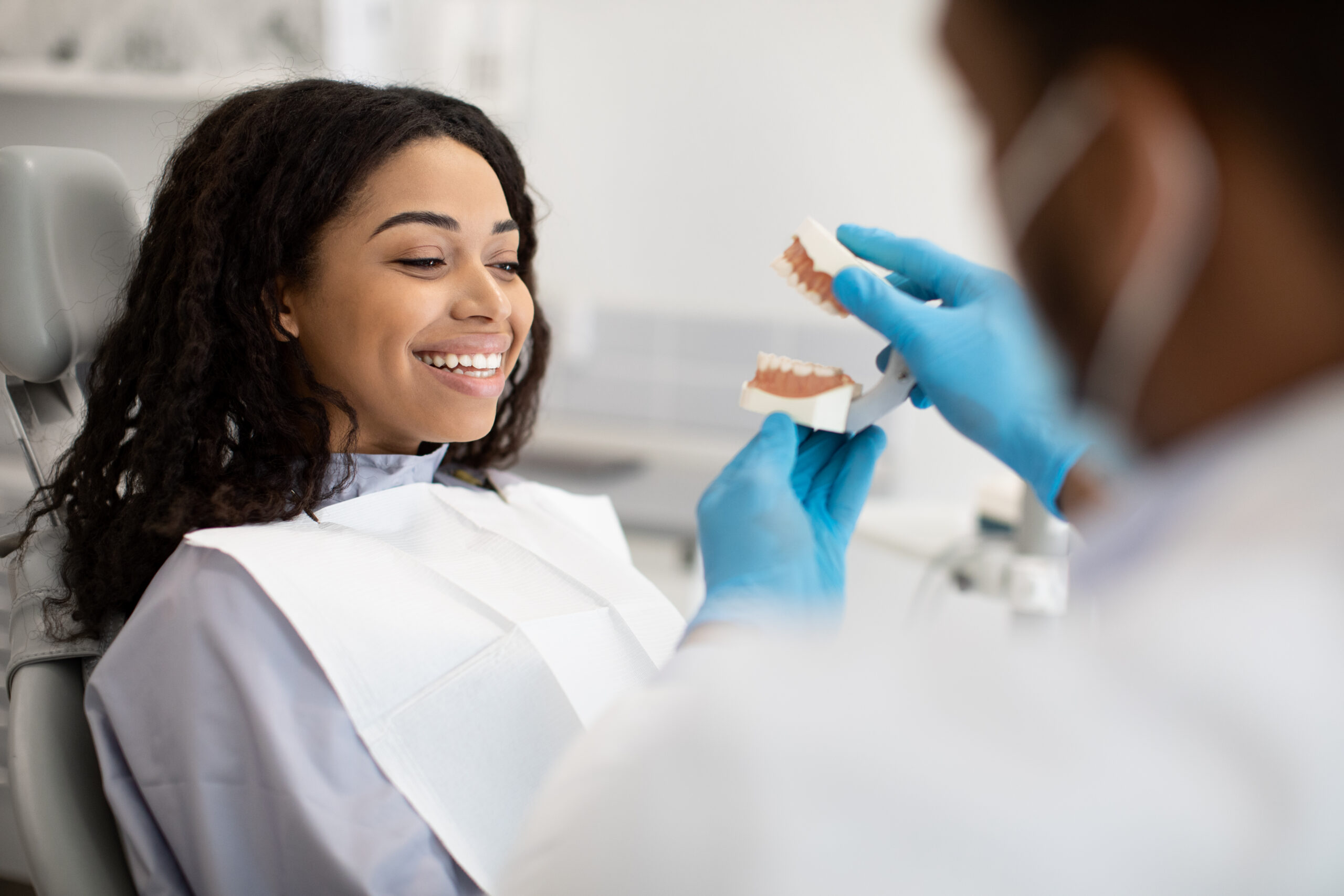 Oral Care. Black Stomatologist Doctor Demonstrating Plastic Jaw To Female Patient